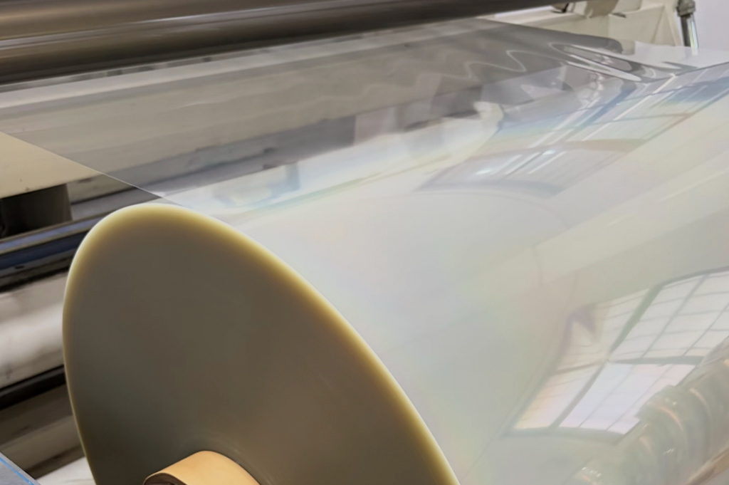Transparent PET polyester film roll being processed on converting machine — high-clarity substrate for premium label and flexible packaging production