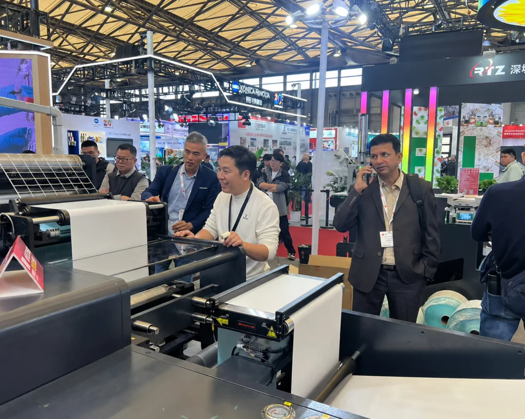 Visitors viewing a label printing machine demonstration at a trade show